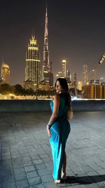 Bia Contrera de vestido azul à noite, com arranha-céus iluminados ao fundo