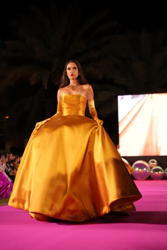 Modelo de vestido dourado volumoso na passarela rosa, à noite